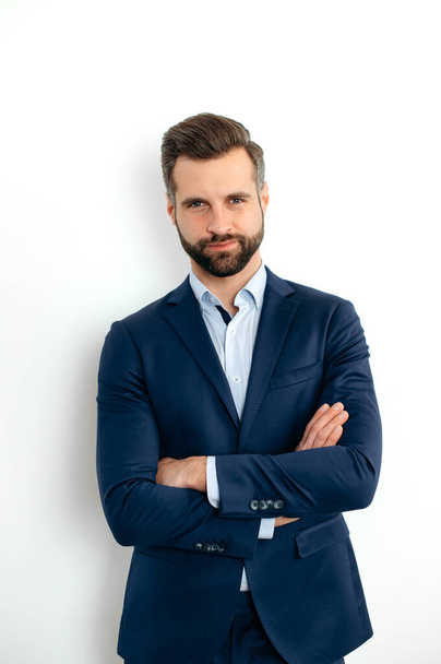 Vertical photo of a proud confident handsome bearded caucasian businessman, corporate executive, in formal elegant suit, stand on isolated white background with arms crossed, looks at camera, smiling - Foto, Bild