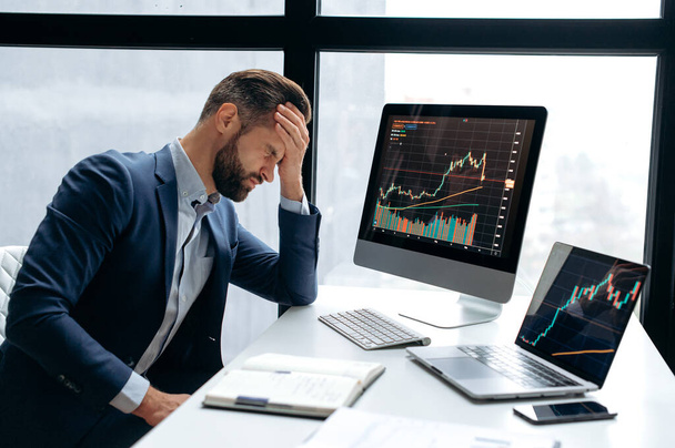 Upset stressed worried caucasian male stock investor, broker, financial expert, sit at work desk in front of computer with charts, nervous of fall cryptocurrency coin, closed eyes, disappointment - Photo, Image