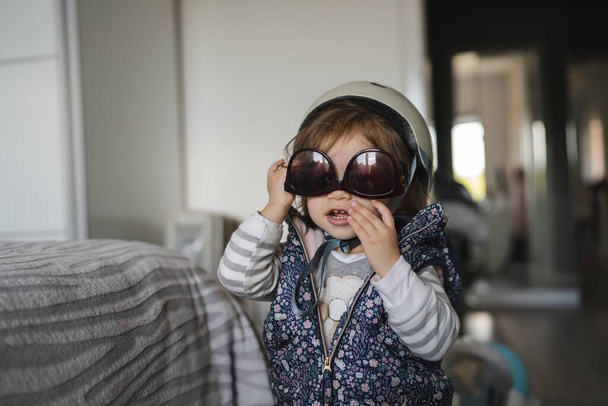 Un petit caucasien fille petit bambin debout un t maison ludique avec casque et lunettes de soleil sur la tête prêt à sortir famille d'enfance et grandir concept copie espace - Photo, image