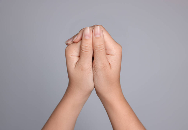 Woman with clasped hands while praying on light grey background, closeup - Foto, Imagem