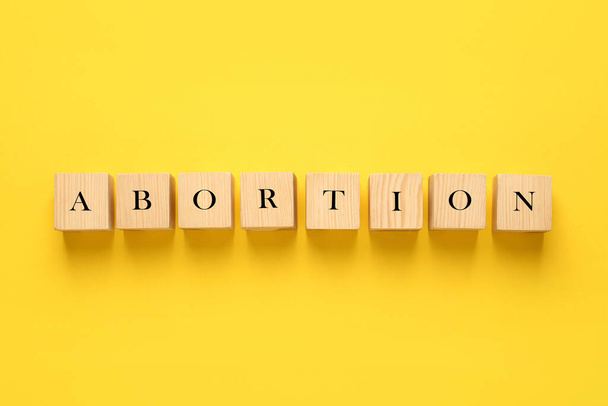 Word Abortion made of wooden cubes on yellow background, flat lay - Photo, image