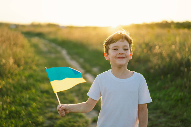 Ukrán Függetlenség Napja. Gyermek fiú fehér pólóban sárga és kék zászlóval Ukrajna területén. Ukrajna zászlója. Az alkotmány napja. Állj ki Ukrajna és mentés - Fotó, kép