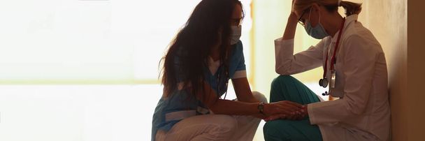 Kobieta lekarz uspokaja zmęczonego kolegę w klinice, zbliżenie. Stres personelu medycznego podczas pandemii - Zdjęcie, obraz