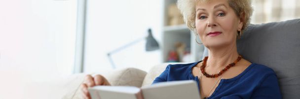 Eine ältere Frau liest zu Hause ein Buch, in Großaufnahme, verschwommen. Rentenalter, Freizeit während einer Pandemie - Foto, Bild
