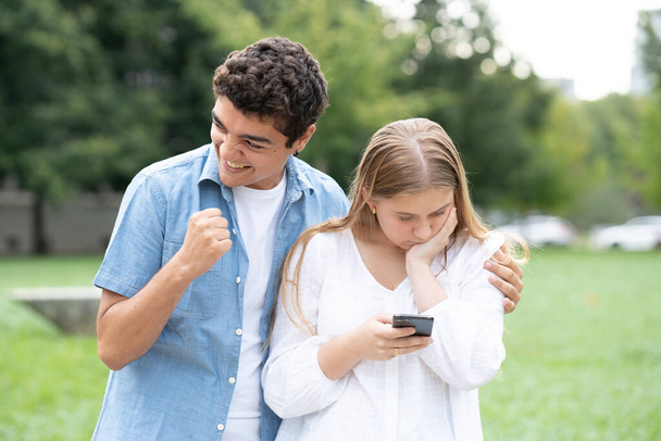 Chica adolescente recibiendo malas noticias por teléfono y niño hipócrita celebrando. Concepto de amistad tóxica - Foto, Imagen