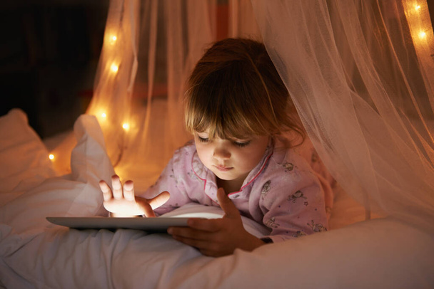 Aufgewachsen im technologischen Zeitalter. Ein junges Mädchen liegt auf ihrem Bett, während sie ein digitales Tablet benutzt - Foto, Bild