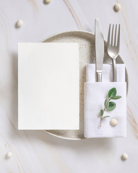 Elegante Tischdekoration mit Karte und Umschlag mit Eukalyptuszweigen von oben, Hochzeits-Mockup. Romantischer Tisch mit vertikaler Papierkarte. Naturverbundenheit und Einfachheit - Foto, Bild