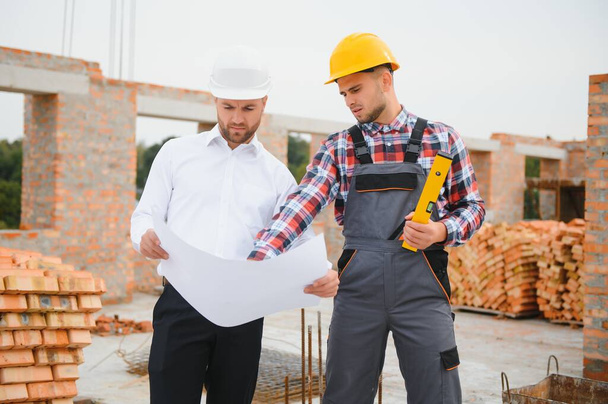 engineer and builder in hard hats discussing blueprint on construction site - Photo, Image