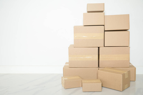 Stack of cardboard boxes for moving, Empty room with a white wall and cardboard boxes with unbranded barcode on the floor. Delivery of goods, shopping. Cardboard boxes on gray wall background. - Foto, Bild