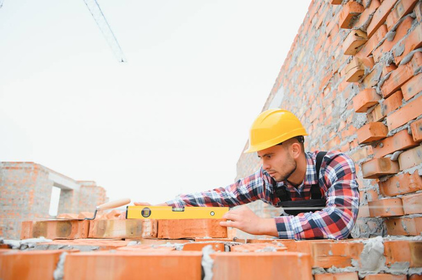 Installing brick wall. Construction worker in uniform and safety equipment have job on building. - Фото, изображение