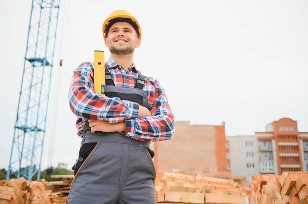 Yellow colored hard hat. Young man working in uniform at construction at daytime - Foto, Imagen