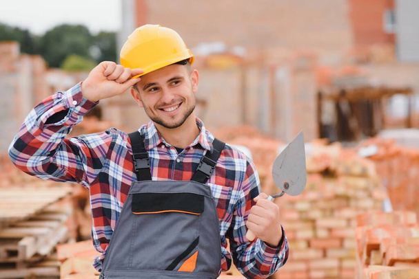 Yellow colored hard hat. Young man working in uniform at construction at daytime - Foto, imagen