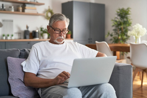 Senior caucasian man sitting at couch and using laptop  - Zdjęcie, obraz