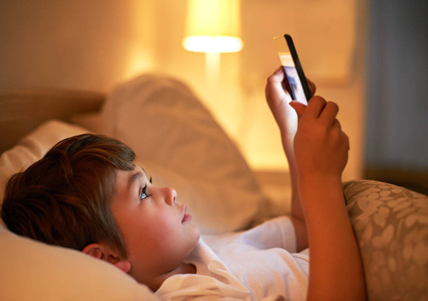 From teddybears to tablets. a young boy using a digital tablet while lying in bed - Foto, afbeelding