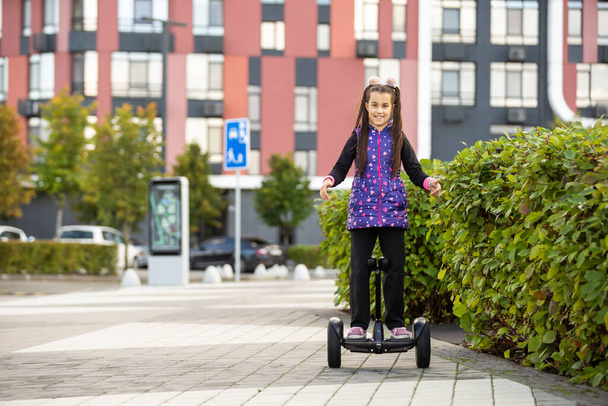 Dışarıda elektrikli scooter 'ın üzerinde duran mutlu küçük kız.. - Fotoğraf, Görsel