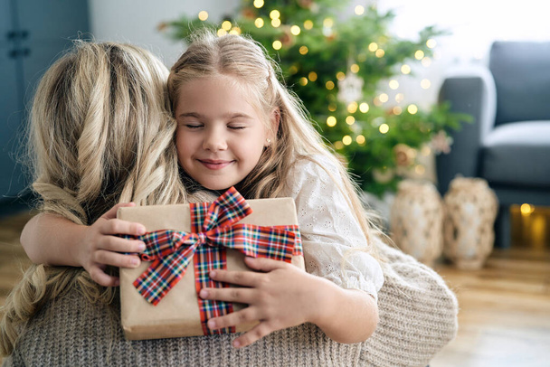 kaukaska mała dziewczynka obejmujący matka i będąc wdzięczny dla jej świąteczny prezent  - Zdjęcie, obraz