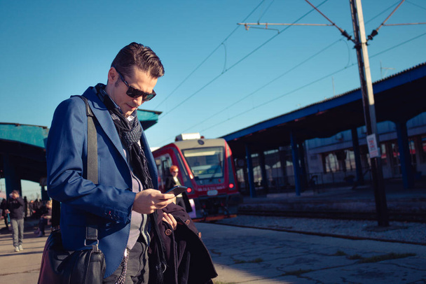 Homme d'affaires utilisant un téléphone portable et vérifiant l'horaire des trains à la gare. - Photo, image