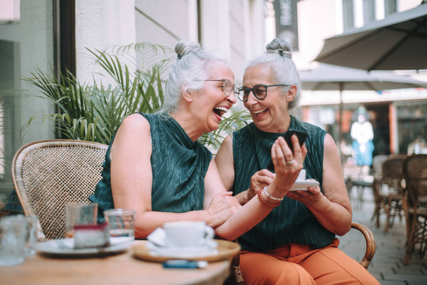 Happy senior women twins having a coffee break in city, smiling and talking. - Фото, зображення