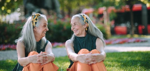 Onnelliset seniorit naiset, kaksoset istumassa puistossa, hymyilemässä ja puhumassa. - Valokuva, kuva