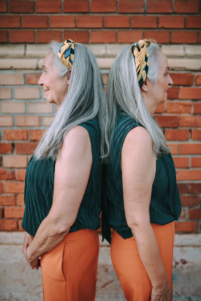 Side view of senior women, twins,in same clothes standing back to back, outdoor in a city. - Fotoğraf, Görsel
