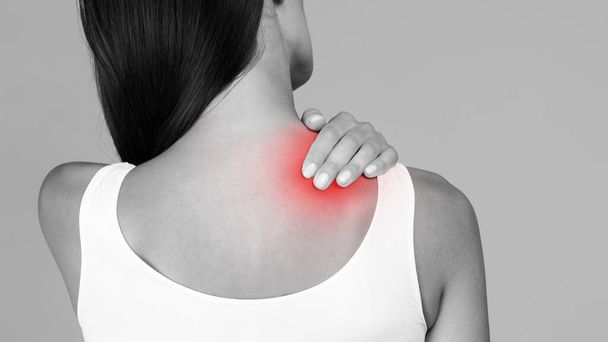Schwarz-Weiß-Foto einer Frau, die starke Rückenschmerzen hat, ihre Schulter massiert und die entzündete rote Zone berührt, Rückansicht, Panorama mit Kopierraum - Foto, Bild