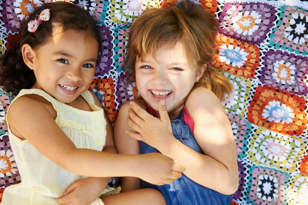 Çocukluk dediğin böyle olur. İki küçük kızın battaniyeye uzanmış oynadığı yüksek açılı bir çekim. - Fotoğraf, Görsel