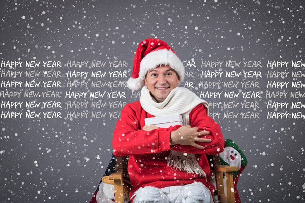 Радостный человек в шляпе Санты держит подарочную коробку, глядя в камеру. С наступающим Новым годом!.  - Фото, изображение