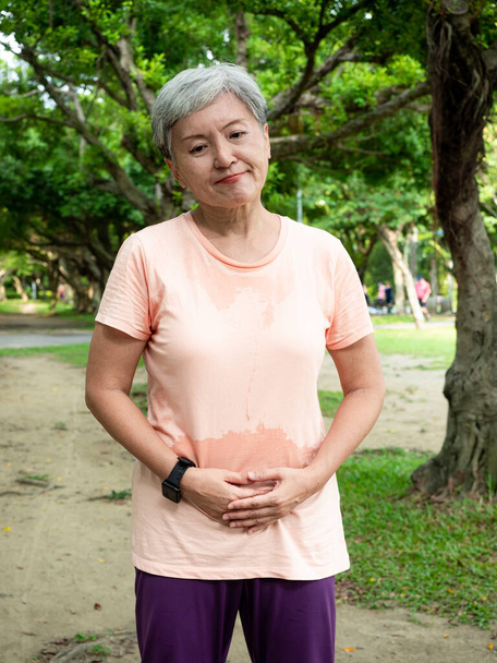 Portré érett ázsiai nő 60-as évek érzés gyomorfájdalom, érintse meg a hasát, szenved a fájdalom a parkban szabadban. - Fotó, kép