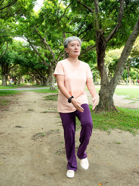 Πορτρέτο της ώριμης γυναίκας της Ασίας 60 τέντωμα πόδια τέντωμα των μυών και να απολαύσετε με τη φύση καθαρό αέρα στο πάρκο. - Φωτογραφία, εικόνα