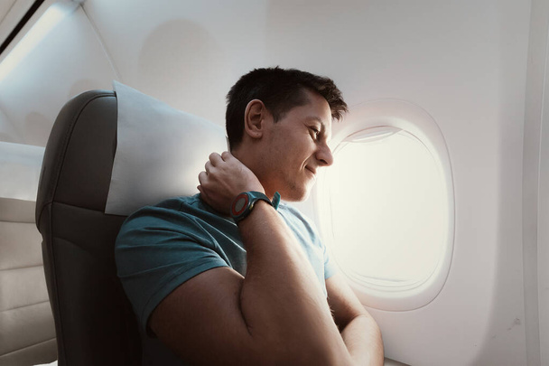 A man suffers from severe neck pain during a long flight in an uncomfortable position on an airplane. Osteochondrosis symptoms and causes - 写真・画像