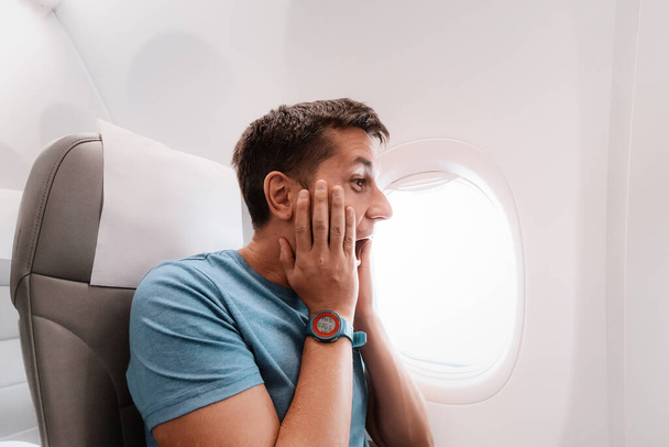 Nuori mies pelkää lentää lentokoneessa ja huutaa emotionaalisesti pelosta. Paniikkikohtaus ja ilmapelko. Tapaturma lennon aikana - Valokuva, kuva