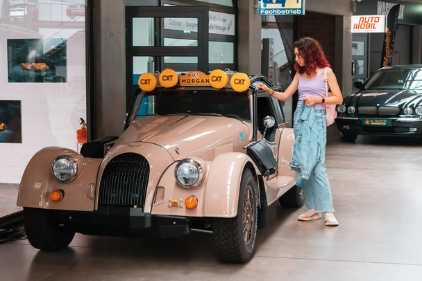 21 July 2022, Dusseldorf, Germany: The girl visitor looks at the exhibits and walks around the museum of retro and modern cars with the possibility of buying - Photo, Image