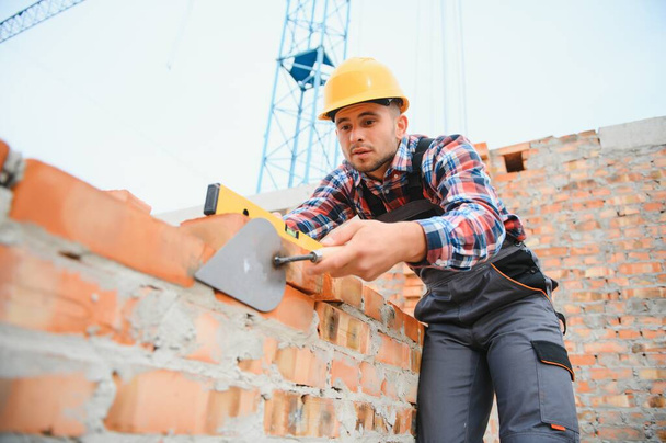 Installing brick wall. Construction worker in uniform and safety equipment have job on building. - 写真・画像