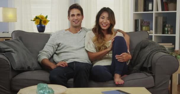 Atractiva pareja de raza mixta sentada en el sofá sonriendo
 - Metraje, vídeo