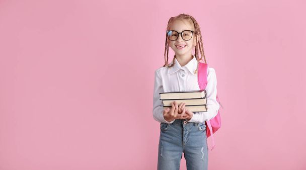 Terug naar school op 1 september concept. Glimlachend schoolmeisje in bril en rugzak heeft boeken over roze achtergrond. schattig kind is op zoek in camera. Leefstijlconcept voor kinderen.Onderwijs op school - Foto, afbeelding