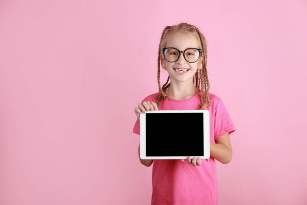 smějící se legrační dítě dívka s tabletem v rukou na růžovém pozadí. Kluk z kavkazské školy v brýlích ukazující prázdnou obrazovku a dívající se do kamery. Prázdná reklama. Zornice propagovat produkt - Fotografie, Obrázek