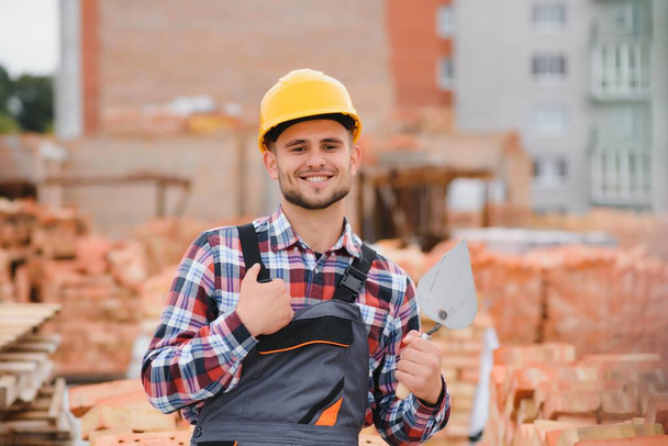 Yellow colored hard hat. Young man working in uniform at construction at daytime - Foto, Imagem