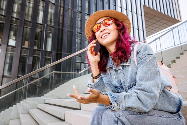 Glückliches Mädchen telefoniert vor dem Hintergrund eines modernen Gebäudes eines Business Centers oder eines Universitätscampus - Foto, Bild