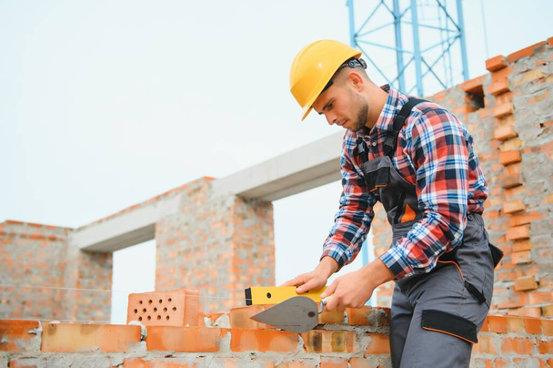 Installing brick wall. Construction worker in uniform and safety equipment have job on building. - Foto, Imagen
