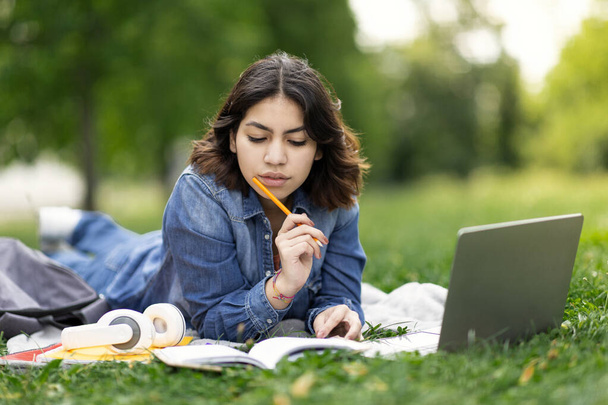 Portrait Of Young Middle Eastern Female Student Preparing For Exam Outdoors, Millennial Arab Woman Lying On Lawn In Park, Study Outside With Laptop Computer And Notepad, Closeup Shot With Copy Space - Photo, Image