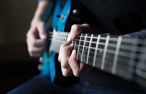 guitarrista tocando la guitarra, un hombre sentado y practicando la guitarra eléctrica sobre fondo oscuro - Foto, imagen