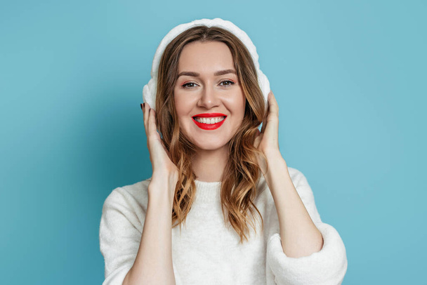 Muotokuva iloinen valkoihoinen nuori nainen talvella turkis kuulokkeet valkoinen pusero hymyillen sininen studio tausta - Valokuva, kuva