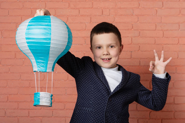 veselý chlapec drží balón v ruce a ukazuje ok gesto druhou rukou, cestovní koncept - Fotografie, Obrázek