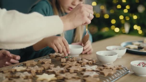 Kaukázusi anya és lánya mézeskalács sütiket díszítenek csokival és cukorral. Lövés RED hélium kamerával 8K-ban.      - Felvétel, videó