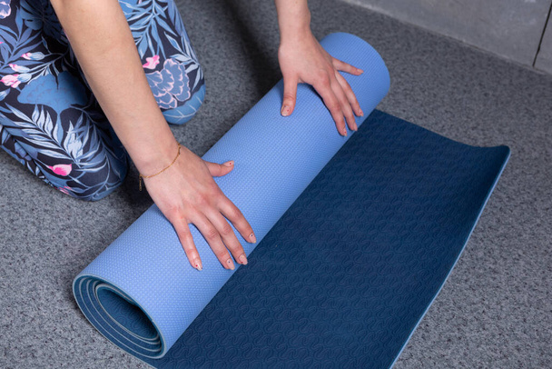 menina desdobra um tapete para ioga ou fitness, mãos e um tapete de close-up, conceito de esporte - Foto, Imagem