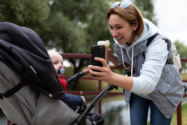 young mother shows a child in a stroller cartoon on the phone. - Photo, Image