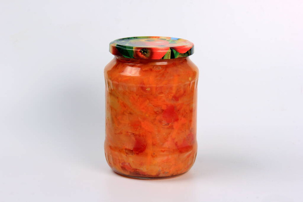 Preparation of canned lecho, canned sweet bell peppers in a glass jar on a white background. Homemade letcho with paprika, tomatoes and carrots - Fotó, kép