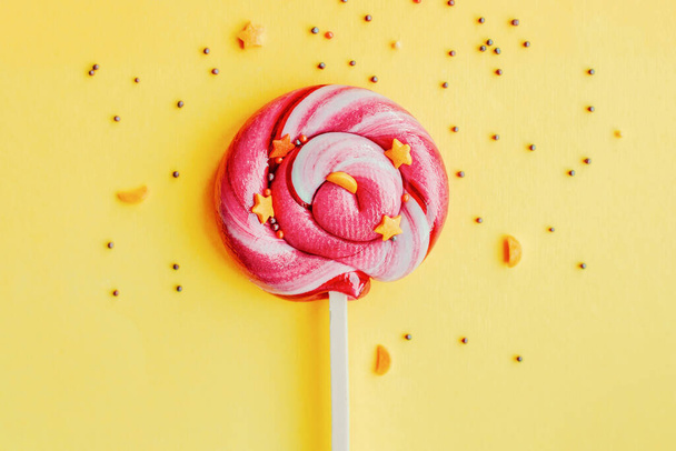 Colorful lollipop with sugar topping isolated over yellow paper background. Flat lay. Copy space. Minimal concept. Close up - Fotografie, Obrázek