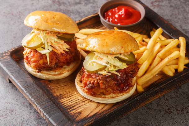 Nashville Hot Chicken is a deep-fried chicken slathered in a spicy paste and served on bun with pickles and coleslaw on top closeup on the tray on the table. Horizonta - Photo, Image