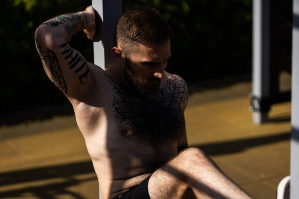 Culturista muscolare bell'uomo con busto nudo si allena tricipiti in una macchina di esercizio cavo crossover sulla strada. - Foto, immagini